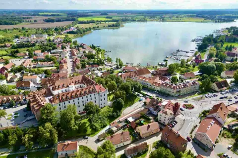 Widok z lotu ptaka na miasteczko nad jeziorem, z zamkiem i licznymi dachami. Idealne punkty widokowe Mazury dla miłośników krajobrazów.