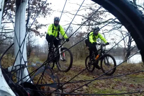 Dwóch rowerzystów w jaskrawożółtych kurtkach przemierza leśny bursztynowy szlak rowerowy.