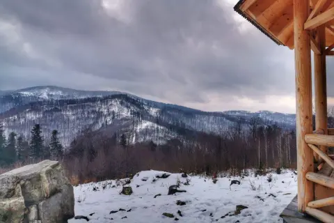 Zimowy krajobraz z ośnieżonymi górami w tle. Na pierwszym planie drewniana altana i kamień. Widok z koziej górki.