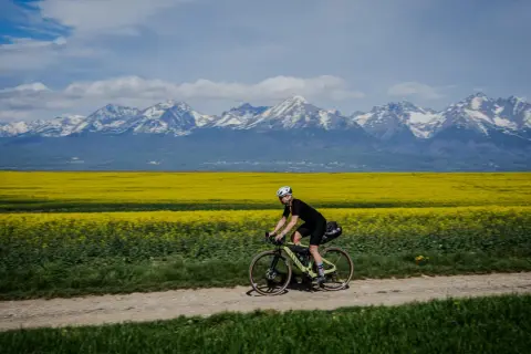 Rowerzystka przemierza polną drogę na tle kwitnącego rzepaku i ośnieżonych Tatr. Marzenie o rowerem dookoła Tatr w jeden dzień staje się rzeczywistością.