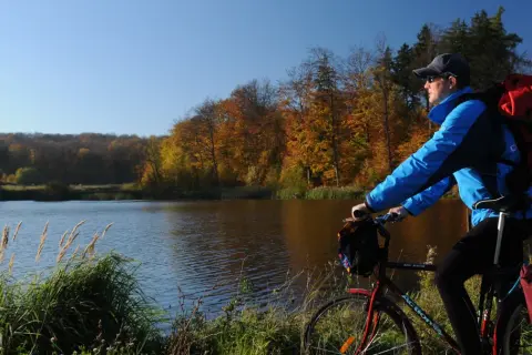 Jesień sprzyja jednodniowym wycieczkom rowerowym. Rowerzysta z plecakiem podziwia jesienne barwy lasu nad jeziorem.