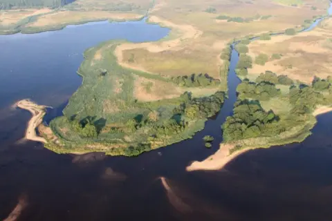Malownicze krajobrazy pomorza gdańskiego: jezioro, kanał, trzciny i piaszczyste brzegi.