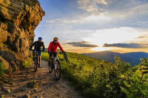 Dwóch rowerzystów przemierza malownicze trasy rowerowe w górach o zachodzie słońca.