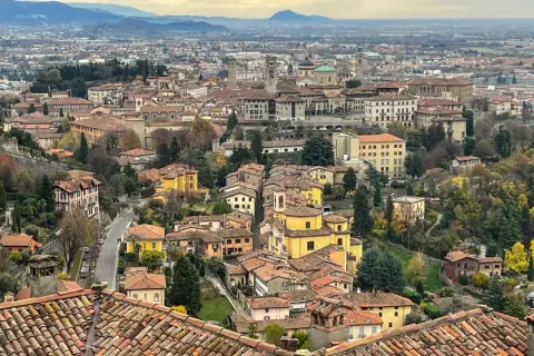 Widok na wzgórza i dachy Bergamo, miasta bliskiego Mediolanowi. W oddali widać góry.
