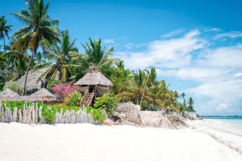 Plaża na Zanzibarze z palmami, chatkami z trawy i drewnianym płotem. Idealne miejsce na wakacje.