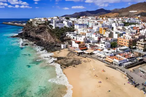 Widok na białe miasteczko na klifie i piaszczystą plażę z turkusową wodą. To urokliwa wyspa Fuerteventura.