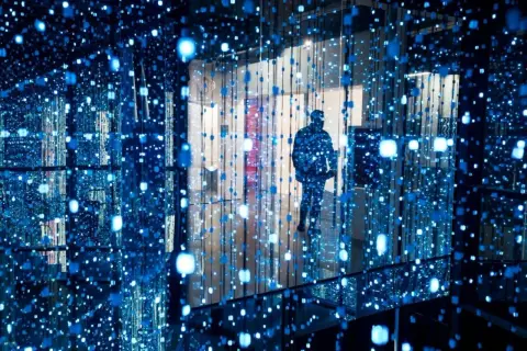 Osoba wchodzi do instalacji świetlnej, jednego z nietypowych miejsc w Warszawie. Błękitne światła tworzą iluzję nieskończoności.