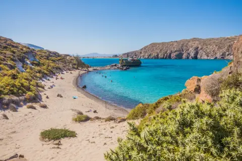 Piękna plaża na wyspie Nisyros z turkusową wodą, łodzią i ludźmi odpoczywającymi na piasku.
