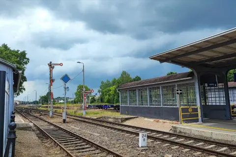 Tory kolejowe na stacji Starogard Gdański pod pochmurnym niebem. Widać peron, budynek poczekalni i semafory.