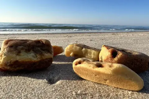 Kilka kawałków bursztynu leży na piaszczystej plaży, z morzem i błękitnym niebem w tle.