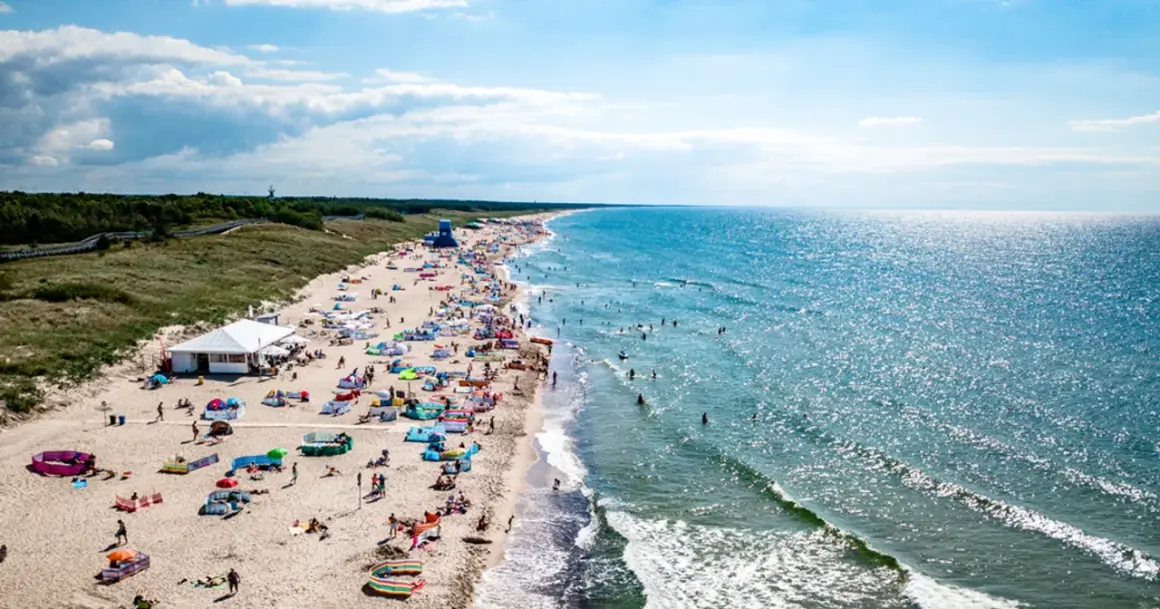 Słoneczna plaża w Darłowie tętni życiem. Tłumy plażowiczów, kolorowe parawany i namioty, a w wodzie kąpielowicze i surferzy. To idealne miejsce na wakacyjne atrakcje.