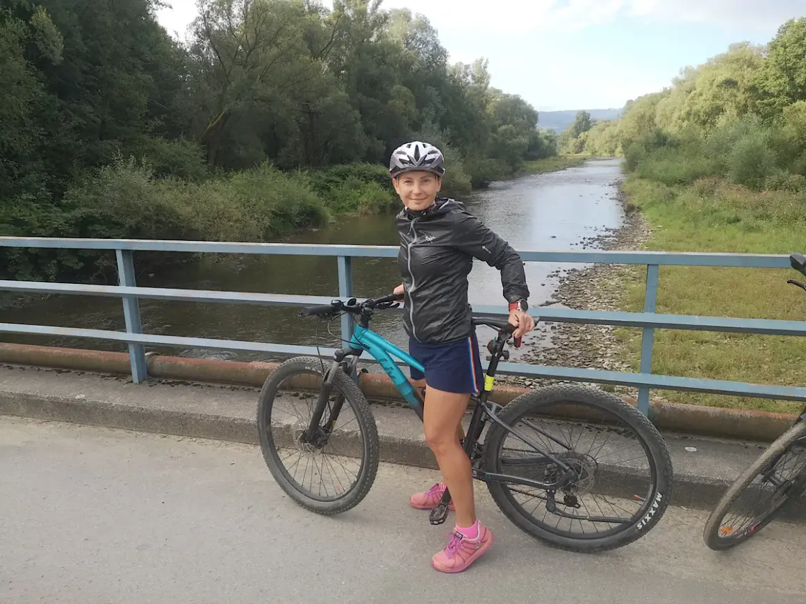 Kobieta na rowerze na moście, gotowa do odkrywania malowniczych velo tras rowerowych wzdłuż rzeki.
