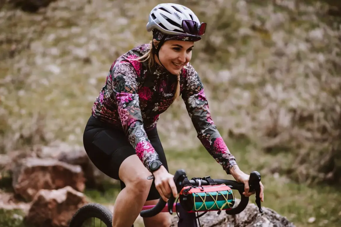 Uśmiechnięta rowerzystka w kwiecistej bluzie pokonuje kolejne kilometry. Dziś czeka ją 50 km na rowerze po malowniczych terenach.