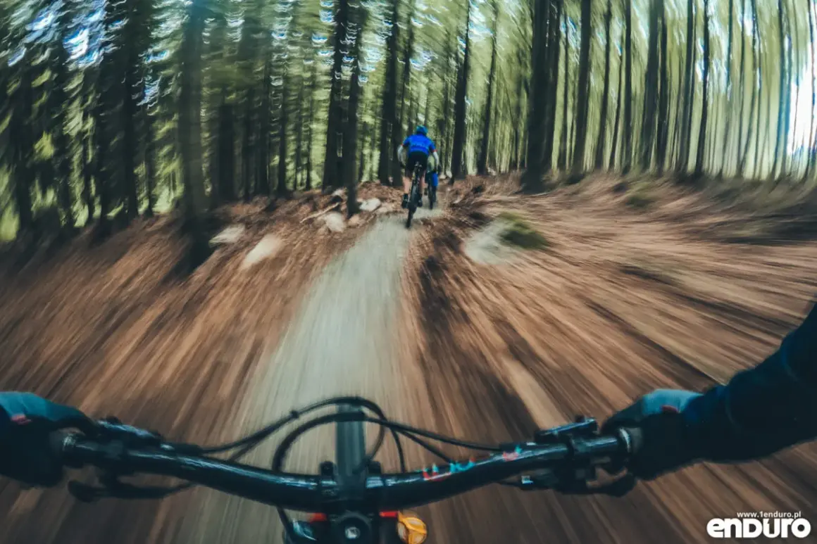 Zjazd rowerowy po leśnym single track glacensis. Widok z perspektywy kierownicy, przed nami inny rowerzysta.