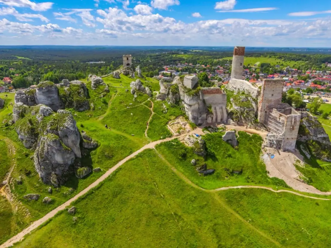 Malowniczy krajobrazowy park orlich gniazd z ruinami zamków na wapiennych skałach, zielone wzgórza i błękitne niebo.