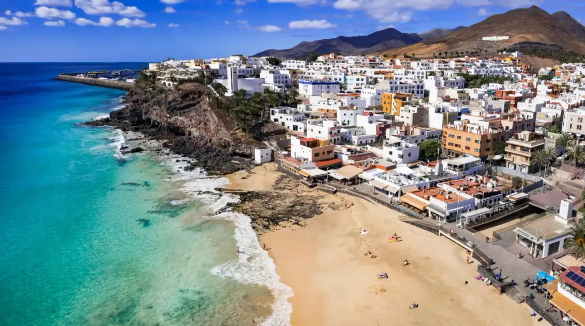 Widok na białe miasteczko na klifie i piaszczystą plażę z turkusową wodą. To urokliwa wyspa Fuerteventura.