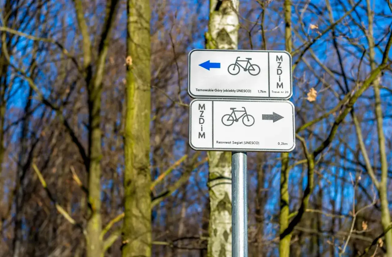 Znaki wskazują szlak rowerowy do Tarnowskich Gór (1,7 km) i Rezerwatu Segiet (0,2 km).