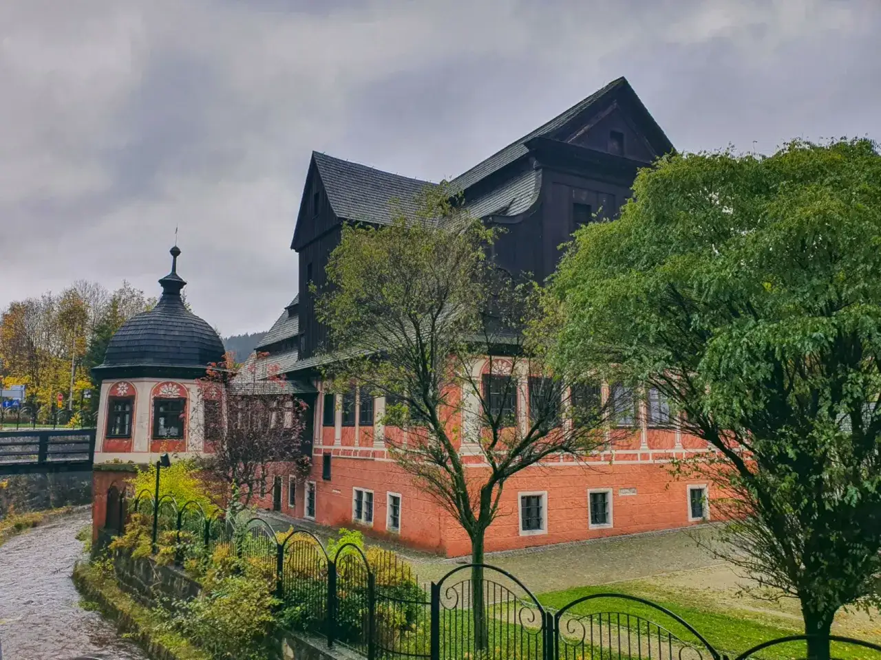 Malowniczy budynek z wieżyczką nad rzeką, otoczony zielenią. Jedna z wielu atrakcji w Dusznikach Zdroju.