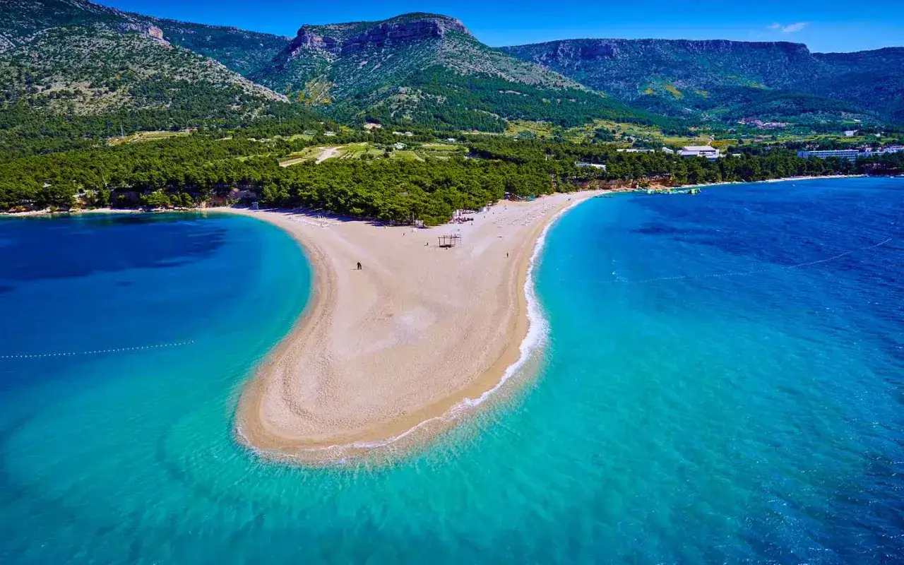 Zlatni Rat, najpiękniejsza plaża w Chorwacji, rozciąga się w turkusowych wodach Adriatyku, otoczona zielonymi wzgórzami.