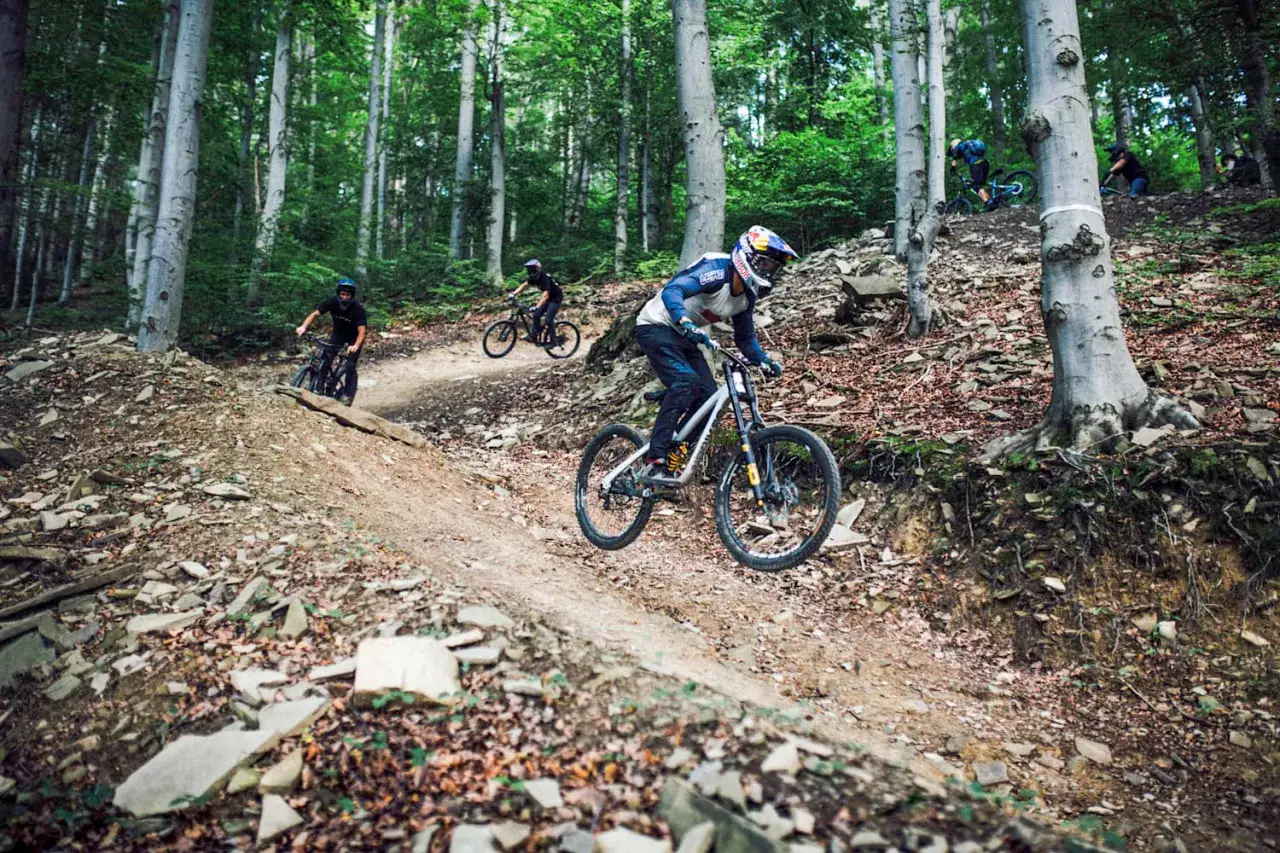 Zjazdowcy na rowerach górskich pokonują kamienisty zjazd w lesie. To adrenalina i świetna zabawa na polskich bike parkach.