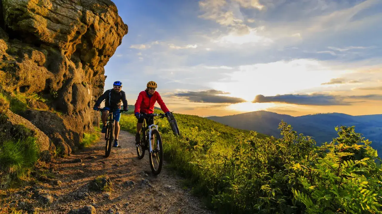 Dwóch rowerzystów przemierza górski szlak o zachodzie słońca. Wspaniałe informacje o rowerze i przygodzie.