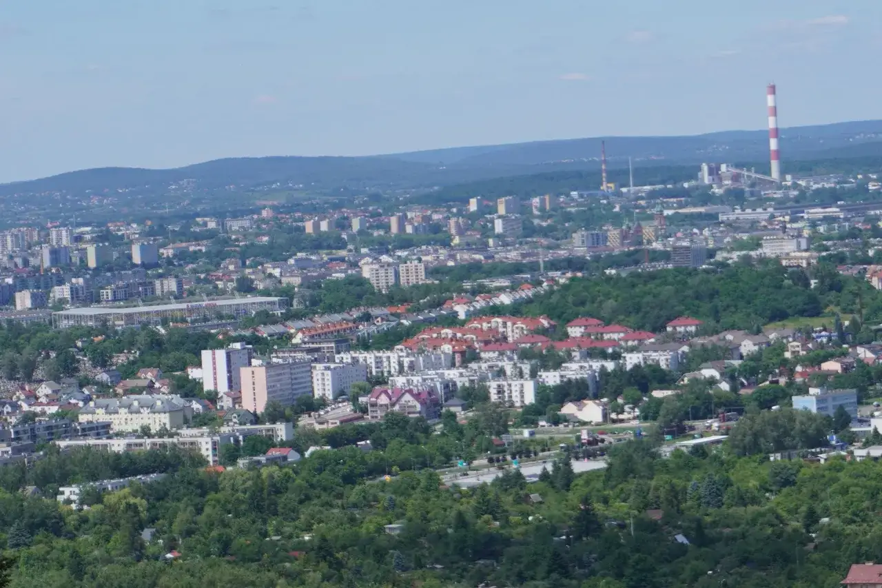 Widok na Kielce w jeden dzień: rozległa panorama miasta z zabudowaniami, zielenią i charakterystycznym kominem.