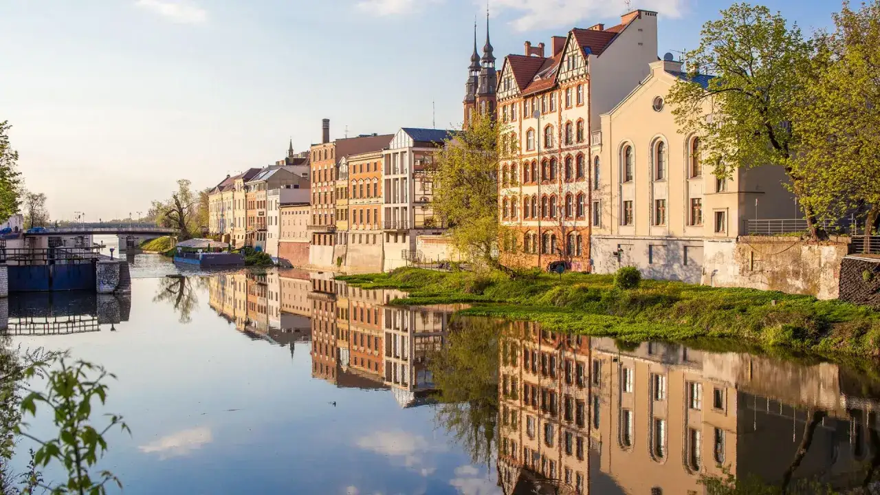 Opole atrakcje: malownicze kamienice nad rzeką Odrą, odbijające się w spokojnej wodzie. Widok na most i śluzę.