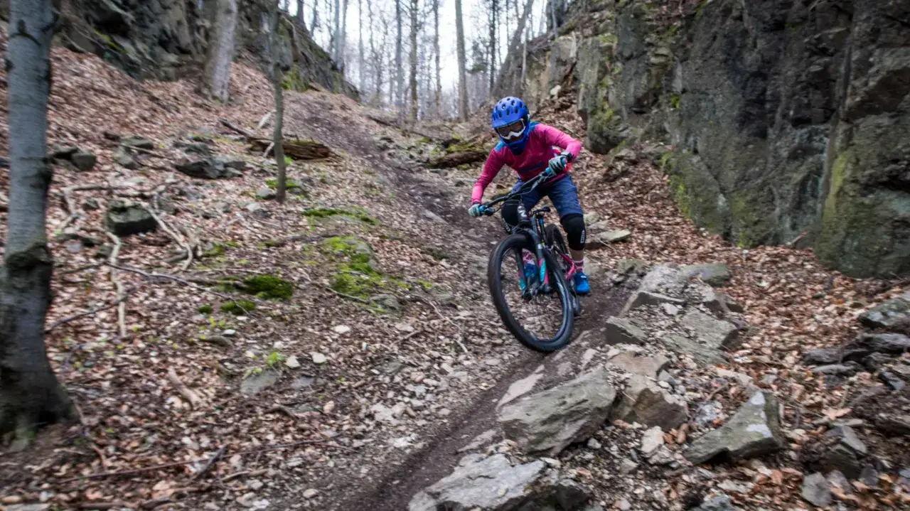 Kobieta w kasku zjeżdża na rowerze enduro po kamienistym, leśnym szlaku.