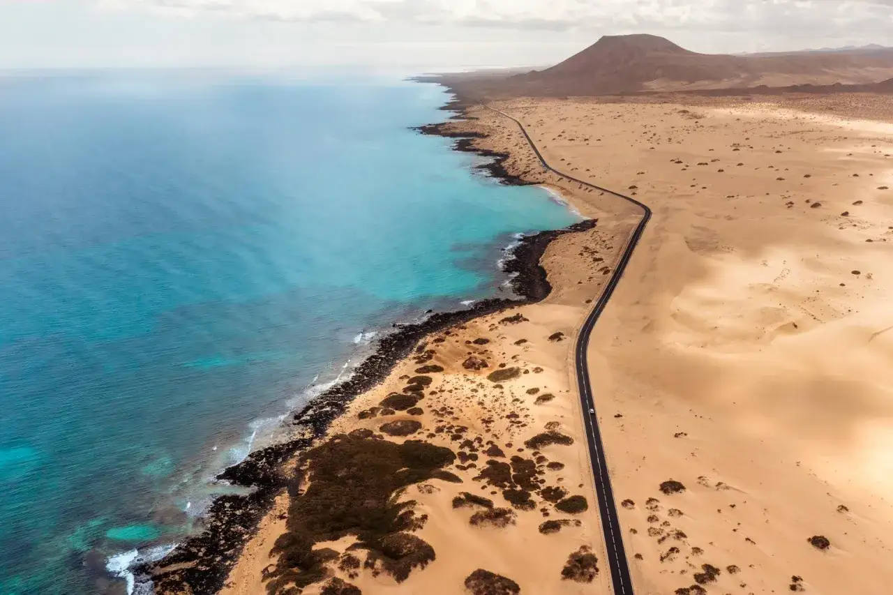 Pustynny krajobraz Fuerteventury z turkusowym oceanem i krętą drogą. Idealne miejsce na zwiedzanie, które inspiruje do stworzenia własnego fuerteventura plan zwiedzania.