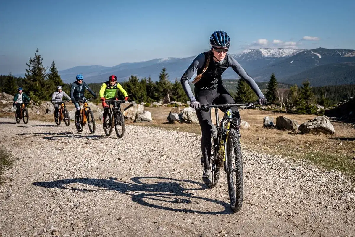 Grupa rowerzystów pokonuje szutrowe trasy rowerowe w Jakuszycach, podziwiając górskie krajobrazy.