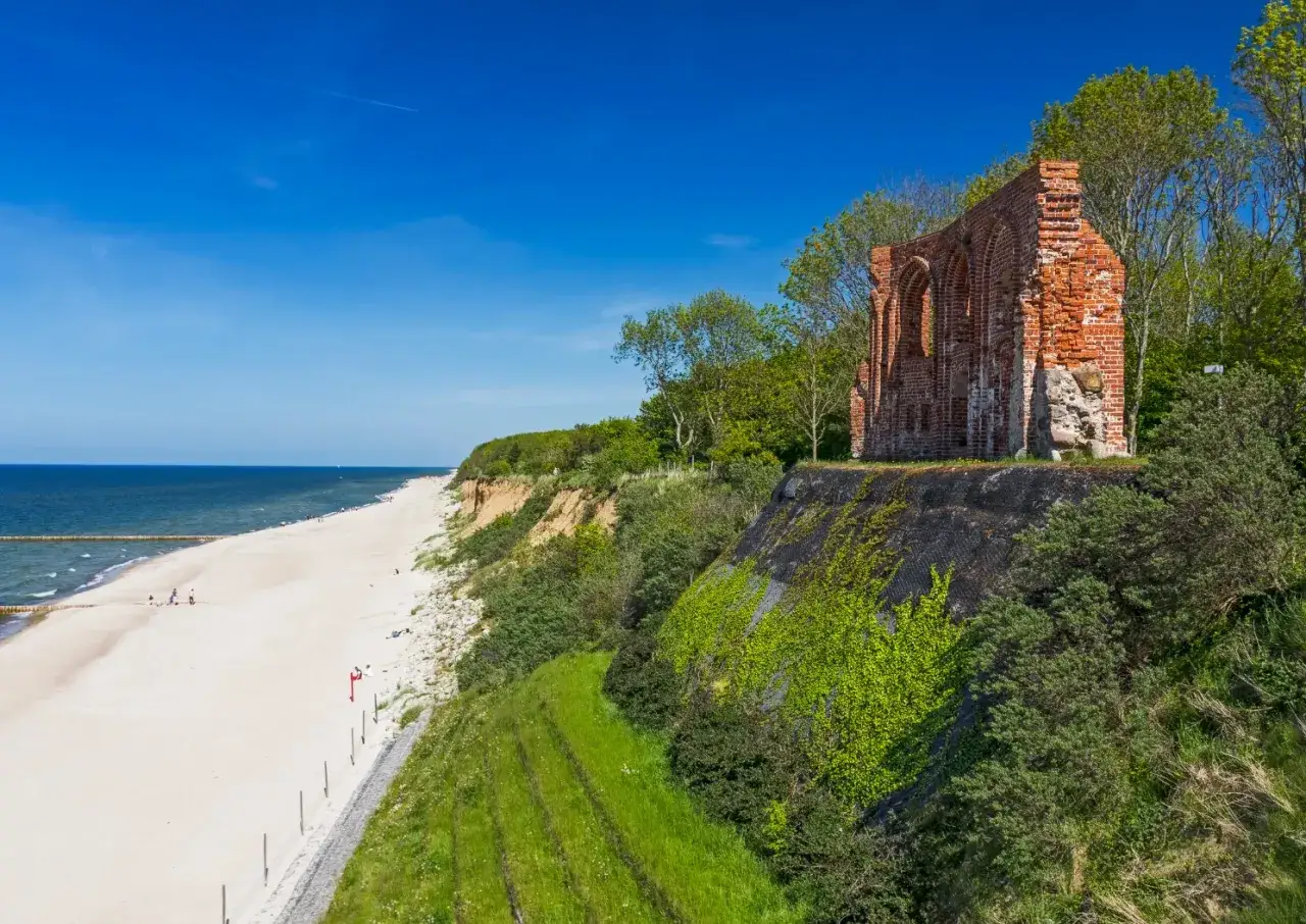 Idealny wyjazd na weekend: ruiny nad morzem, piaszczysta plaża i błękitne niebo.