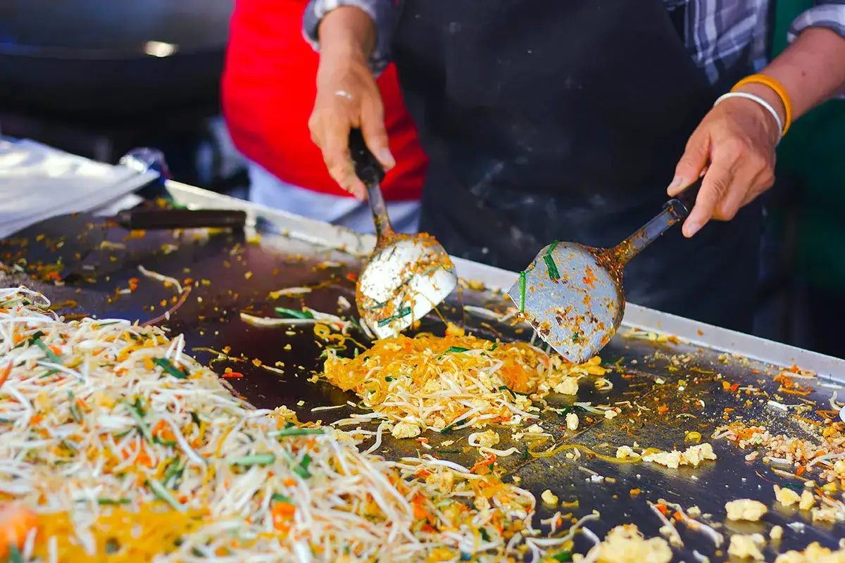Ręce przygotowują Pad Thai na ulicy Khao San. Makaron, kiełki fasoli i jajka smażą się na gorącej płycie.